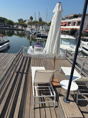 A wooden deck with lounge chairs and an umbrella, overlooking a marina with boats. - Renovated marina in Port-Camargue – Dock, large terrace, air conditioning, 51 m² (Le Grau-du-Roi)