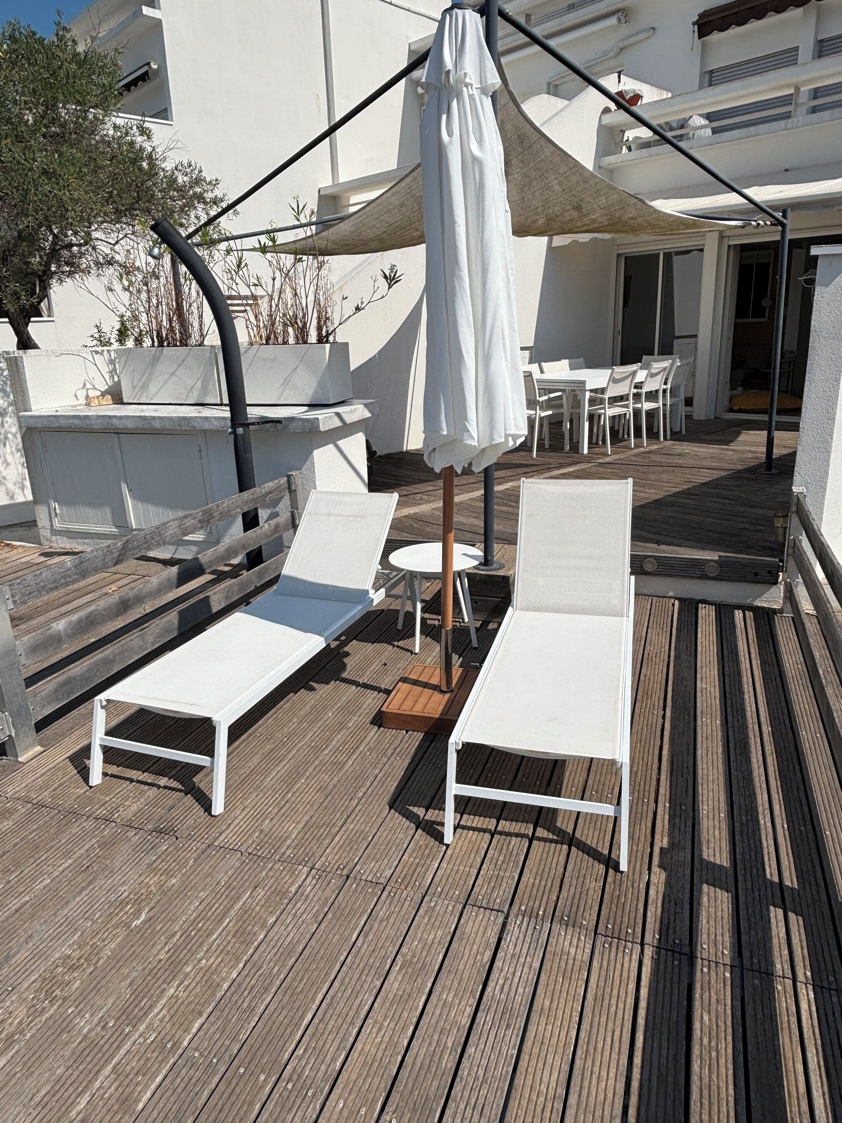 A rooftop terrace with white lounge chairs and a table, a canopy, and a view of the surrounding buildings.