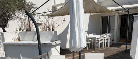 Terraza en la azotea con sillones blancos, una mesa, una toldo y vistas de los edificios circundantes.