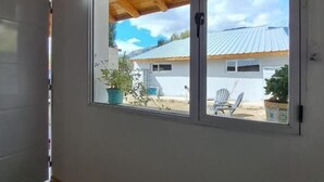 Une pièce dotée d’une grande fenêtre, de poutres apparentes en bois au plafond et offrant une vue sur un bâtiment et sur du mobilier d’extérieur.
