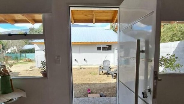 Une pièce avec un plafond en bois, une porte blanche et une vue sur un jardin avec une chaise et une table.