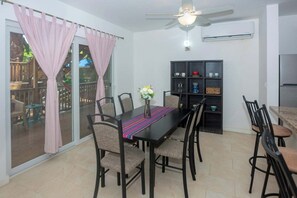 Ein Essbereich mit Tisch, Stühlen, Deckenventilator und einer Glaswand mit Vorhängen.