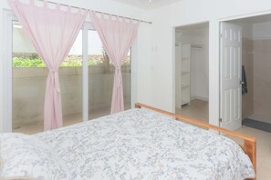 Une chambre à coucher avec un lit, une porte-fenêtre coulissante donnant sur un balcon et une porte ouverte menant à une salle de bain.