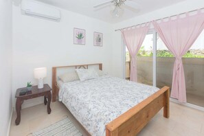 Ein Schlafzimmer mit Bett, Nachttisch, Lampe und Blick ins Freie.