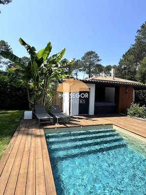 A pool area with lounge chairs and a wooden deck. - Villa Murmur - Seignosse - Pool - Jacuzzi (Seignosse)