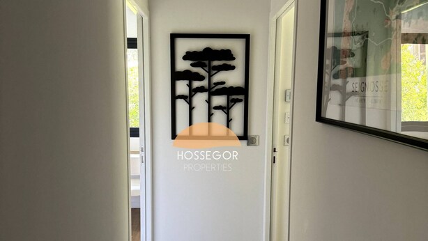 Un pasillo con un cuadro enmarcado de árboles, un mapa enmarcado y un cartel de 'HOSSEGOR PROPERTIES'.