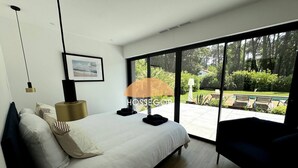 Un dormitorio moderno con una cama grande, una mesita de noche, una lámpara y vistas a un jardín por un ventanal corredero.