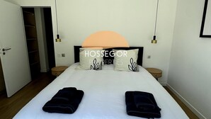 Un dormitorio con una cama grande, dos mesitas de noche, un armario y una puerta que da a otra habitación.
