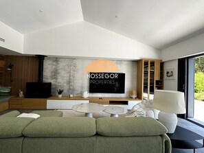 Ein modernes Wohnzimmer mit Flachbildfernseher, Holzschrank, Sofa und Essbereich.