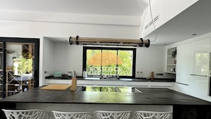 Una cocina moderna con una isla grande, sillas blancas y vistas al exterior.