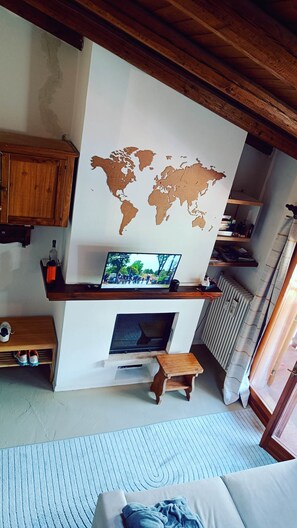 A room with a world map on the wall, a television, a fireplace, a wooden bench, and a bed. - Appartamento Monti e sole (Folgarida)
