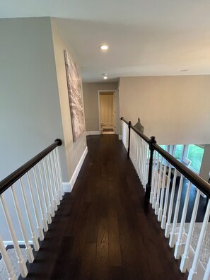 A hallway with a wooden floor, white railings, and a door at the end.