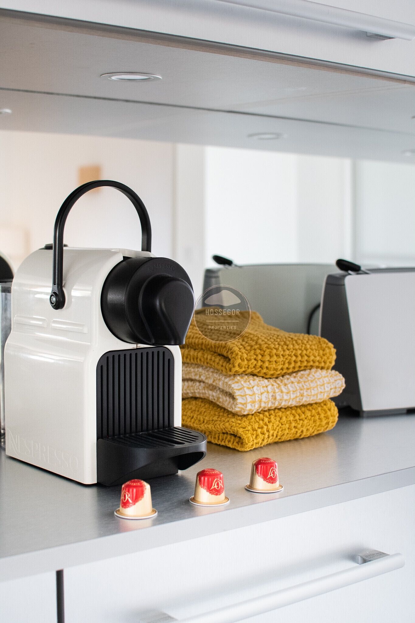 Una cocina con cafetera, una pila de toallas dobladas y un tostador.