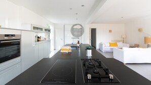 Et moderne køkken med en central ø, indbygget ovn og spiseplads med en hvid sofa.