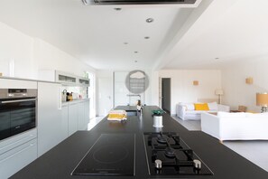 Eine moderne Küche mit einer zentralen Kochinsel, einem eingebauten Backofen und einem Essbereich mit einem weißen Sofa.