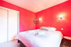 A hotel room with a bed, pillows, a bedside table, and a wall-mounted lamp. - Villa Her Den - Hossegor - Town center - Lake (Soorts-Hossegor)