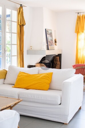 Ein weißes Sofa mit einem gelben Kissen, ein weißer Sessel und ein kleiner Tisch mit Kerze und Bilderrahmen auf einem Regal.