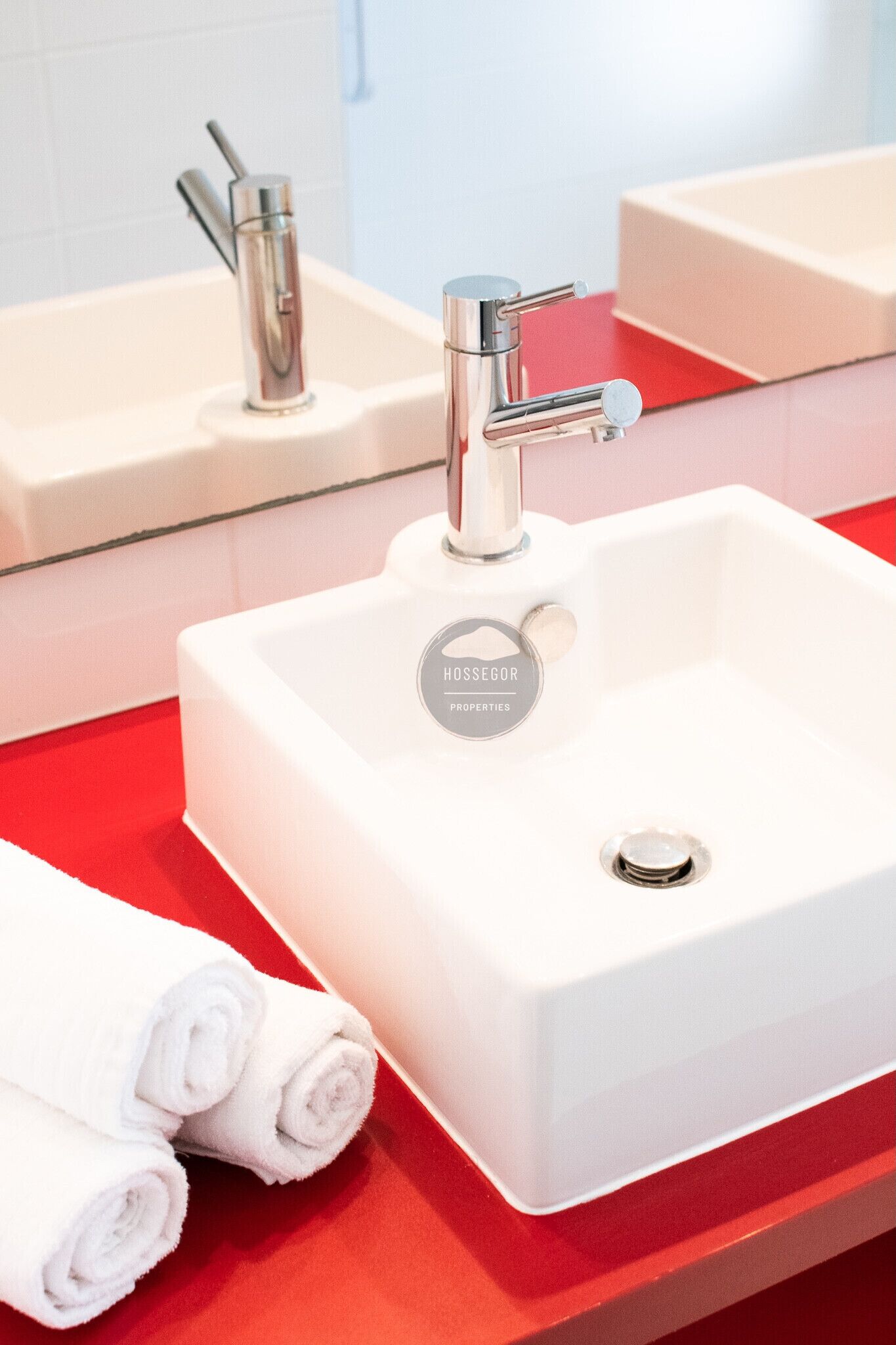 A bathroom with a white sink, a mirror, and a red countertop.