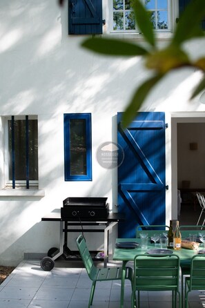 A patio with a grill, a table with chairs, and a blue door. - Villa Her Den - Hossegor - Town center - Lake (Soorts-Hossegor)