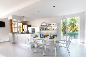 A modern kitchen with white cabinets, a central island with seating, and a dining area with a table and chairs. - Villa Her Den - Hossegor - Town center - Lake (Soorts-Hossegor)