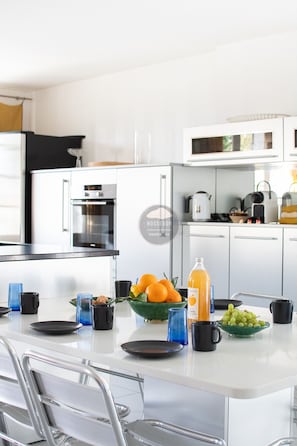 A modern kitchen with white cabinetry, a stainless steel oven, and a dining area with a glass table. - Villa Her Den - Hossegor - Town center - Lake (Soorts-Hossegor)