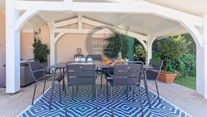 Eine Terrasse im Freien mit Tisch, Stühlen, einem Grill und Kübelpflanzen.