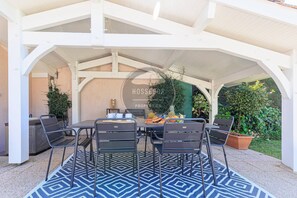 Eine Terrasse im Freien mit Tisch, Stühlen, einem Grill und Kübelpflanzen.