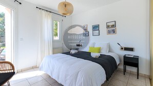 Ein Schlafzimmer mit einem Bett, Nachttischen, einem Sessel, einem Fenster und einem Wandbild.