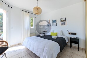 Ein Schlafzimmer mit einem Bett, Nachttischen, einem Sessel, einem Fenster und einem Wandbild.