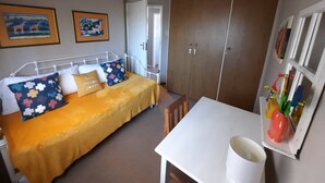 A bedroom with a bed, a white table, and a wardrobe. There are two paintings on the wall. - Amazing View For Less Bloubergstrand Beachfront (Cape Town)