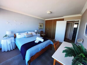 A bedroom with a bed, bedside tables, a desk, and a wardrobe. - Amazing View For Less Bloubergstrand Beachfront (Cape Town)