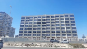 A multi-story building with a uniform facade, a gated entrance, and a clear blue sky. - Amazing View For Less Bloubergstrand Beachfront (Cape Town)