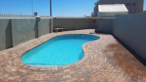 A swimming pool with a brick border, a street lamp, and a gated fence. - Amazing View For Less Bloubergstrand Beachfront (Cape Town)