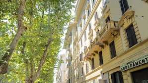 A street lined with multi-story buildings, some with balconies, and trees with green leaves.
