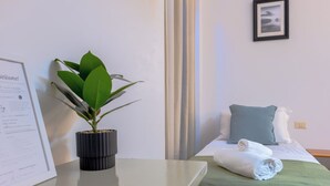 A hotel room with a bed, a rolled towel, a green throw, a potted plant, and a welcome sign.