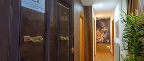 Un pasillo con puertas de madera, un cartel en la pared y una planta en maceta.