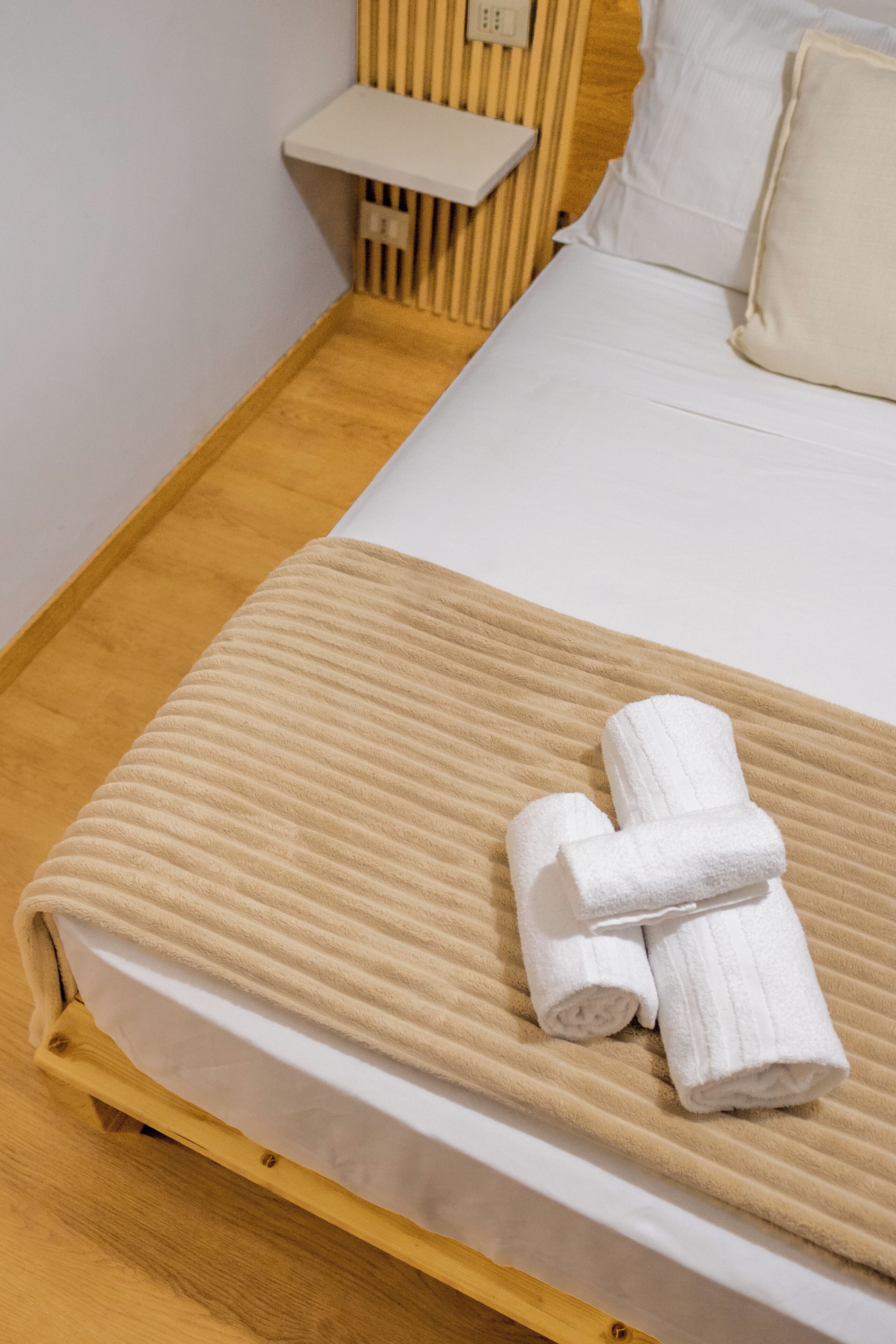 A neatly made bed with a beige blanket and rolled white towels.