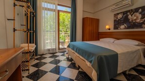 Ett hotellrum med ett rutmönstrat golv, en säng med ett blått överkast, en garderob i trä, en väggmonterad luftkonditioneringsanläggning och ett fönster med gardiner.