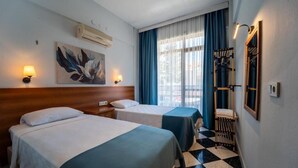 Ett hotellrum med två sängar, en tavla på väggen, ett fönster med gardiner, en trästol och ett rutigt golv.