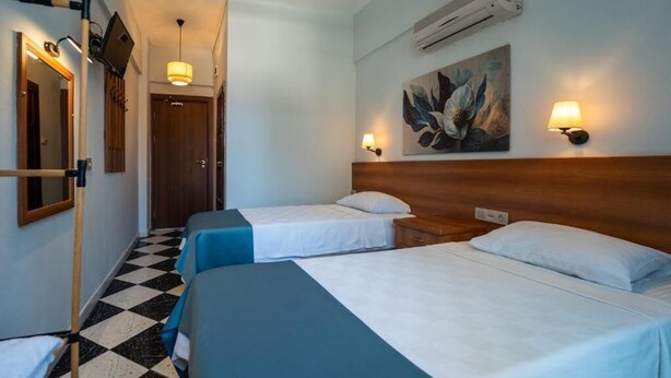 Ett hotellrum med två sängar, ett rutmönstrat golv, en tavla på väggen och en väggmonterad luftkonditioneringsanläggning.