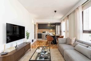 A modern living room with a flat-screen TV, a sofa, a coffee table, and a dining area with a table and chairs. - Apartamento de 2 habitaciones totalmente reformado y equipado, situado en Calle Juan Álvarez Mendizábal, a un paso de la Plaza de España, el Templo de Debod y Gran Vía (MADRID)