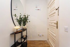 A hallway with a mirror, a potted plant, a table with a lamp, and a door with a handle. - Apartamento de 2 habitaciones totalmente reformado y equipado, situado en Calle Juan Álvarez Mendizábal, a un paso de la Plaza de España, el Templo de Debod y Gran Vía (MADRID)