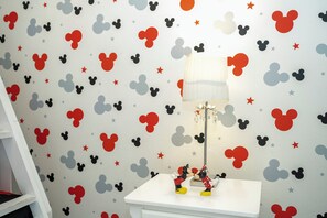 Ein Zimmer mit Wandgestaltung zum Thema Mickey Mouse, einem weißen Nachttisch und einer Lampe.