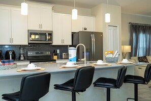A modern kitchen with white cabinets, stainless steel appliances, and a bar area with black chairs. - The best 5 bedrooms Storey Lake - 10 min DIsney (Kissimmee)