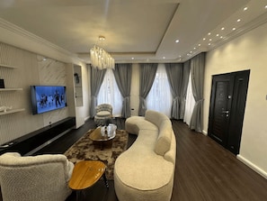 Ein modernes Wohnzimmer mit einer Couch, Sesseln, einem Couchtisch und einem an der Wand montierten Fernseher.