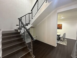 Eine Treppe mit schwarzer Geländer, die zu einer oberen Etage führt, eine weiße Wand mit einem Bild und ein Essbereich mit Tisch und Stühlen.