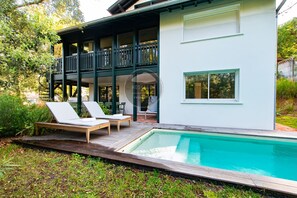 Ein modernes, zweistöckiges Haus mit Pool, Sitzgelegenheit im Freien und einem Balkon.