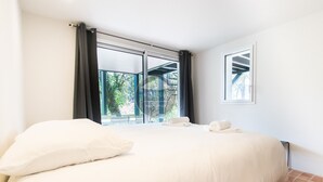 Quarto de hotel com cama grande, duas almofadas, janela com cortinas e vista para o verde lá fora.