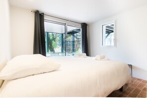 Ein Hotelzimmer mit einem großen Bett, zwei Kissen, einem Fenster mit Vorhängen und Blick ins Grüne.