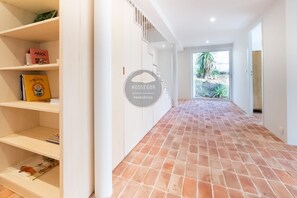 A hallway with a tiled floor, white walls, and a door leading to a balcony with a view of greenery. - Villa Analoma - Seignosse - Pool - Beach (Seignosse)